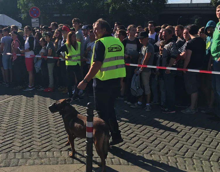 Sicherheitskraft mit Diensthund vor einer Warteschlange